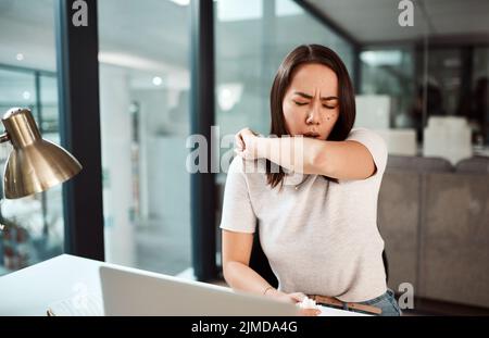 Pratica buona etiquette tosse per il bene della salute di tutti. Una giovane donna d'affari tosse nel suo gomito in un ufficio. Foto Stock