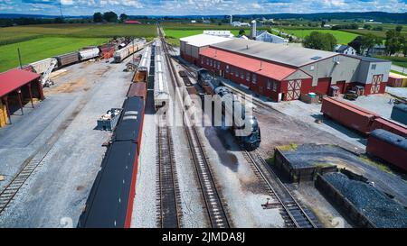 Vista aerea di un antico motore a vapore restaurato che soffia fumo e vapore nel Freight Yard Foto Stock