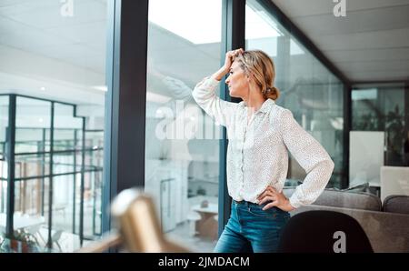 Una volta ero motivata nella mia carriera, una donna d'affari matura che guarda stressata fuori in un ufficio. Foto Stock
