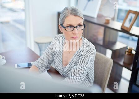 Ponderando sopra una decisione che deve fare. Una donna d'affari matura che osserva pensieroso mentre lavora su un calcolatore in un ufficio. Foto Stock
