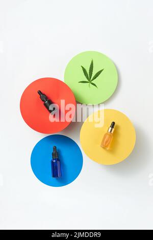 Tessere rotonde colorate con bottiglie di olio CBD di cannabis su sfondo grigio chiaro. Foto Stock