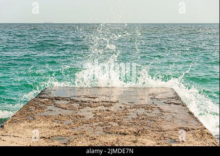 Mare â€ â€€ le onde si rompono con gli spruzzi sul molo di frangiflutti vicino alla costa Foto Stock