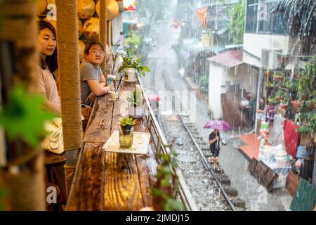 Hanoi, Vietnam. 30th luglio 2022. I turisti si affacciano da un balcone alle piogge monsoniche che adrenano la famosa "strada dei treni" di Hanoi. Quasi tre anni dopo la chiusura della famosa 'Train Street' nella capitale del Vietnam Hanoi, la vista popolare come selfie spot è di nuovo aperto. (A dpa: 'Popolare 'Train Street' in Hanoi aperto di nuovo - ma non ufficialmente') credito: Chris Humphrey/dpa/Alamy Live News Foto Stock