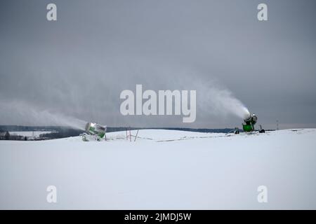Macchina per la innevamento sulle piste da sci in inverno. Spruzzare polvere di neve. Ruscello bianco di neve sullo sfondo del cielo nuvoloso. Foto Stock