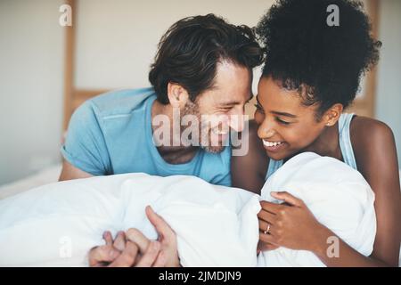 Felice, amorevole e divertente coppia interrazziale sorridendo e ridendo mentre si sdraia a letto e condividendo un momento tenero. Spensierato marito e moglie rilassante e. Foto Stock