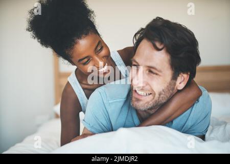 Interrazziale, divertente e amorevole coppia coccolare a letto e godersi il fine settimana insieme a casa. Affettuoso, felice e che lega gli amanti diversi Foto Stock