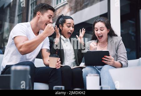 Il successo ha un sapore ancora migliore quando avete fame. Un gruppo di giovani uomini d'affari eccitati che usano un tablet digitale durante una riunione a una conferenza. Foto Stock