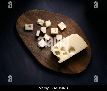 Formaggio con buchi tagliati a cubetti su tavola di legno Foto Stock