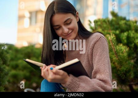 Donna sorridente che legge il giornale personale sulla strada Foto Stock