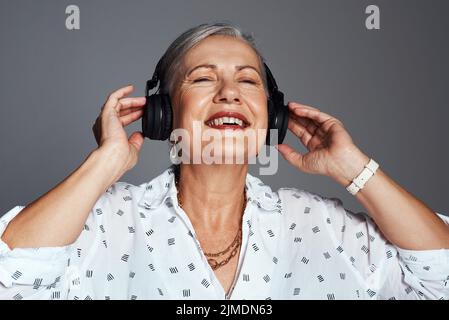 Vi garantisco che la musica vi farà sentire meglio. Studio girato di una donna anziana indossando le cuffie mentre ascolti la musica contro un grigio Foto Stock