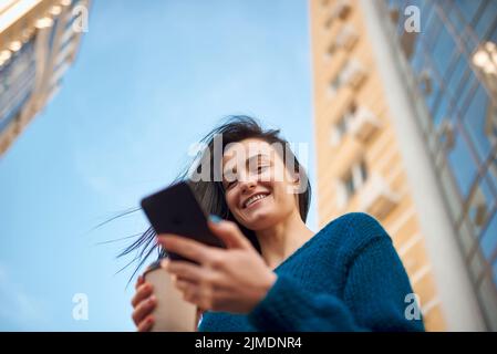Donna sorridente con smartphone è circondata da edifici alti Foto Stock