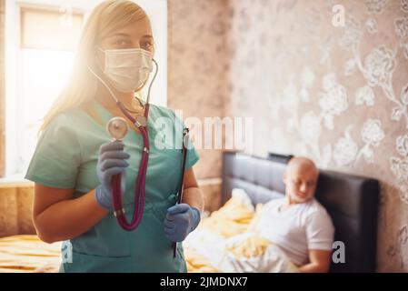 Chiamata casa. Visita del medico a casa. Esame del paziente. Ritratto di un'infermiera che indossa maschera, guanti e stentoscopio Foto Stock