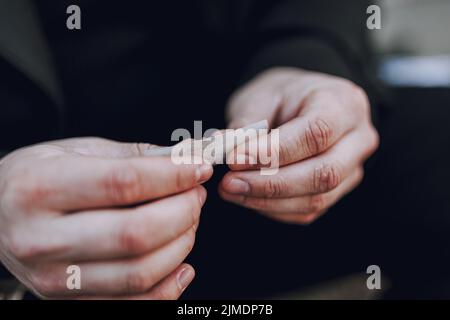 Mani maschili che arrotolano una sigaretta di tabacco all'aperto Foto Stock