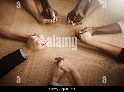 Gruppo di uomini d'affari diversi che tengono le mani insieme in solidarietà su un tavolo. Colleghi in unità che si sostengono a vicenda, la preghiera nella Foto Stock