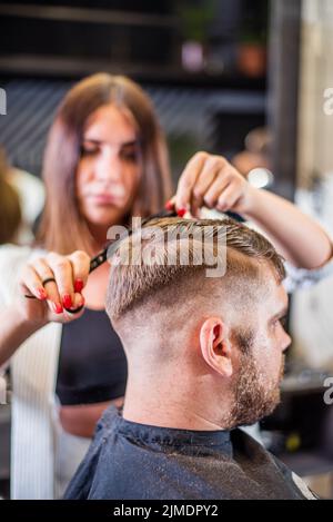 Donna parrucchiere che taglia con le forbici un uomo bearded in un barbiere Foto Stock