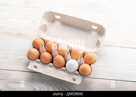 Un uovo bianco circondato da uova marroni. Concetto di individualità, unicità e diversità. Vista dall'alto con spazio di copia. Foto Stock