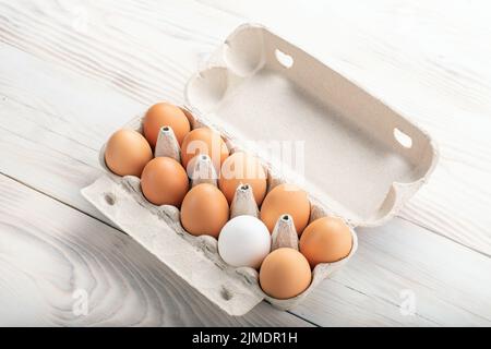 Uova rosolate e tra loro un uovo bianco in scatola di cartone. Concetto di differenza, dissimilarità, sconosciuto. Spazio per il testo Foto Stock