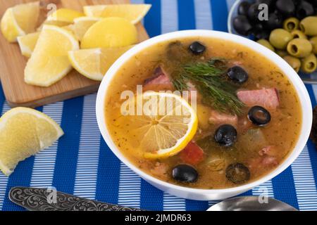 Zuppa con carne, olive, limone, condimenti e spezie su sfondo blu. Solyanka russa, cibo fatto in casa. Vista dall'alto. Foto Stock