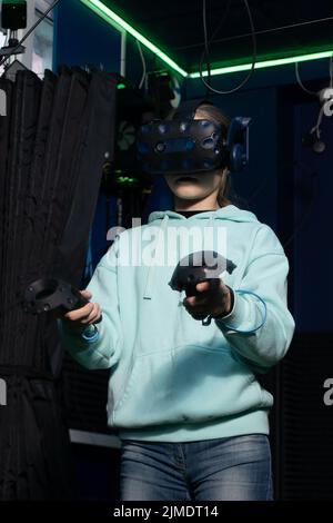 Ragazza con visore per realtà virtuale che utilizza il joystick mentre gioca a un videogioco nel club di gioco vr. Foto Stock