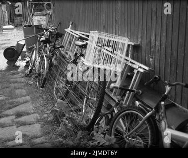 collezione di biciclette usate appoggiate al muro in un caotico cortile, in bianco e nero Foto Stock