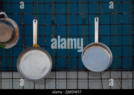 le padelle in ghisa sono appese alle griglie sul muro, gli utensili da cucina sono nuovi e puliti Foto Stock