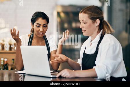 Come abbiamo fatto a correre in perdita: Due donne che usano un computer portatile insieme mentre lavorano in un bar. Foto Stock