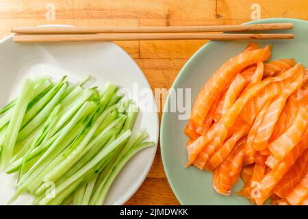 Vista dall'alto di salmoni e cetrioli freschi su piatti e bastoncini di bambù. Foto Stock