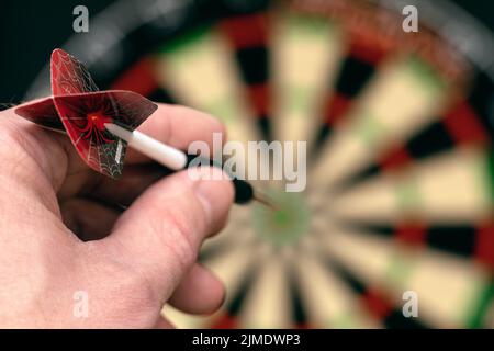 La mano dell'uomo tiene la dardo e mira al bersaglio. Realizzare gol. Gioco di freccette. Foto Stock