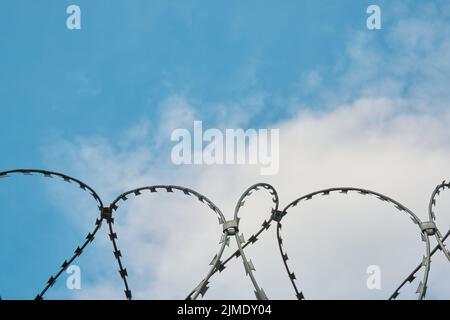 Filo spinato su uno sfondo di cielo blu e bianco nuvole Foto Stock