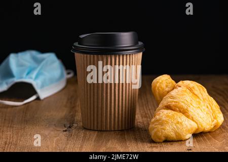 Vista laterale di deliziosi croissant con caffè caldo da portare a casa in tazza usa e getta di carta. Foto Stock