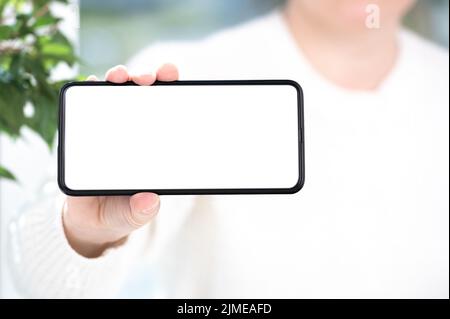 Cellulare mockup. Donna in abiti bianchi mostra bianco cellulare schermo bianco in posizione orizzontale. Donna mano tenendo e mostrando nero cellulare intelligente Foto Stock