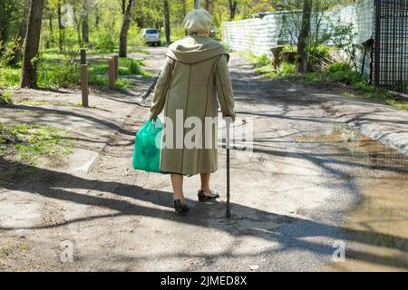 Il pensionato cammina lungo la strada. Nonna in Russia. Donna con bastone da passeggio. Uomo anziano in città. Foto Stock