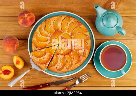 Torta fatta in casa con pesche e tazza di tè su tavola di legno. Vista dall'alto. Foto Stock