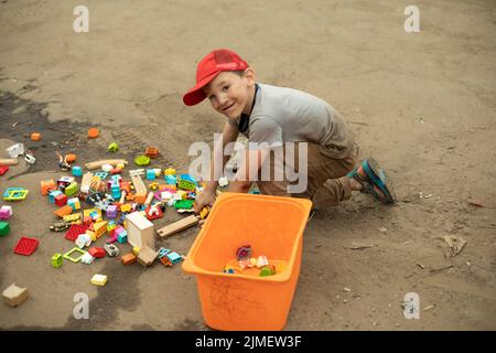 Bambino con scatola di giocattoli. Giocattoli sparsi per ragazzo. Bambini in strada. Foto Stock