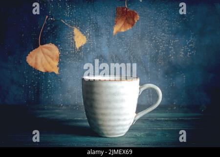 Giornata piovosa con una tazza di tè. Foglie autunnali, pioggia dietro la finestra Foto Stock