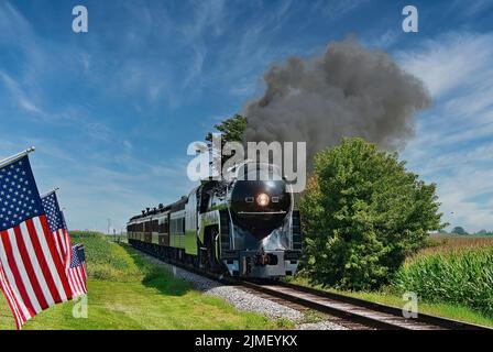 Antico motore a vapore restaurato che si avvicina testa passando una fila di bandiere americane Foto Stock