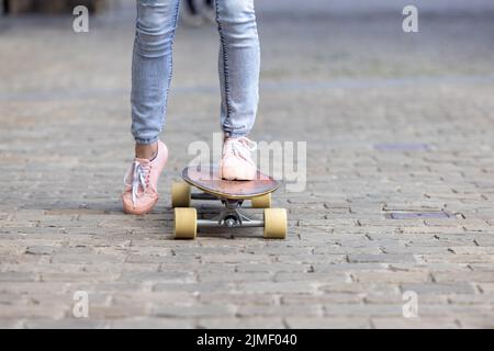 Tiro corto di giovani gambe donna in sneakers pratica nuovi trucchi allo skateboard nel parco. Concetto di sport e stile di vita urbano Foto Stock