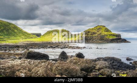 Turisti sul sentiero Giants Causeway con vista sulla costa rocciosa e le scogliere Foto Stock