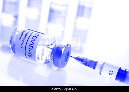 Flaconcino di vetro con etichetta di vaccino del coronavirus insieme alla siringa closeup, colore blu, foto Foto Stock