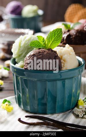 Tre cucchiai di pistacchio di vaniglia e palline di gelato al cioccolato in ciotole di argilla su tavolo da cucina in legno Foto Stock