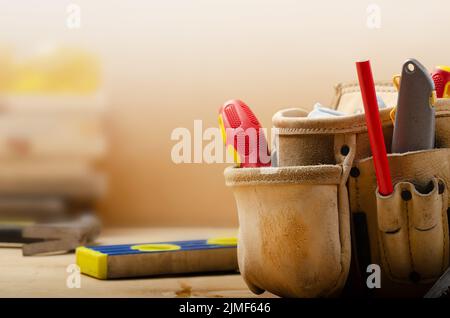 Cintura portautensili in pelle gialla con attrezzi su compensato con piano e occhiali di sicurezza a lato Foto Stock