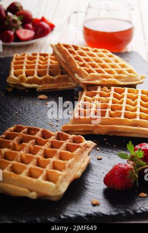 Waffle belgi fatti in casa su vassoio di ardesia con sciroppo d'acero e. fragole da parte Foto Stock