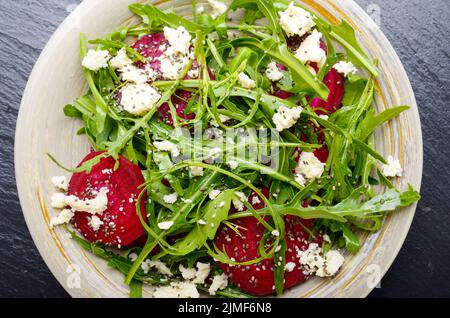 Vista da sopra al piatto di argilla con barbabietole rosse foglie di rucola e formaggio feta insalata su pietra ardesia vassoio vista ingrandita Foto Stock