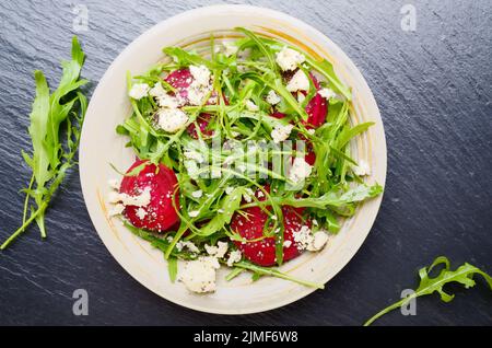 Vista da sopra al piatto di argilla con barbabietole rosse foglie di rucola e formaggio feta insalata su pietra ardesia vassoio vista ingrandita Foto Stock