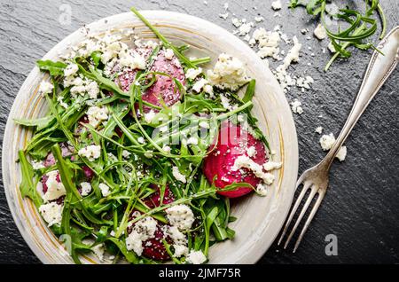 Vista da sopra al piatto di argilla con barbabietole rosse foglie di rucola e formaggio feta insalata su pietra ardesia vassoio closeup vista. Forcella a parte Foto Stock