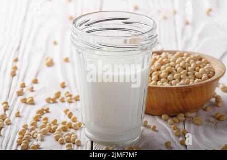 Non a base di latte di soia alternativa latte o yogurt a mason jar bianco sul tavolo di legno con i fagioli di soia in un recipiente a parte Foto Stock