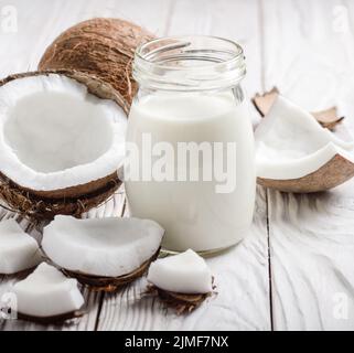 Latte o yogurt a mason jar su bianco tavolo in legno con noce di cocco a parte Foto Stock