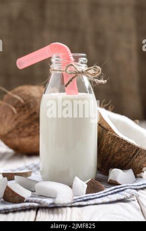 Bottiglia di vetro di latte o yogurt sul tovagliolo blu su bianco tavolo in legno con noce di cocco a parte Foto Stock