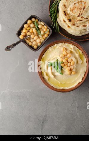 Piatto Hummus laici in piatto di argilla condito con ceci e foglie di coriandolo verde su tavola di pietra servita con pane tradizionale Pita Foto Stock