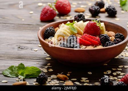 Frutto sano muesli con banana fragola mandorle e blackberry nel piatto di argilla su legno tavolo da cucina Foto Stock